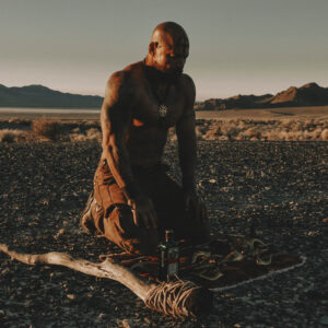 Man kneeling on a desert plain at sunset beside an arrangement on the ground