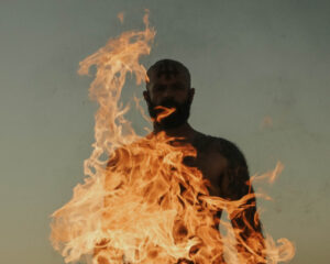 Silhouette of a man standing behind a column of fire at dusk