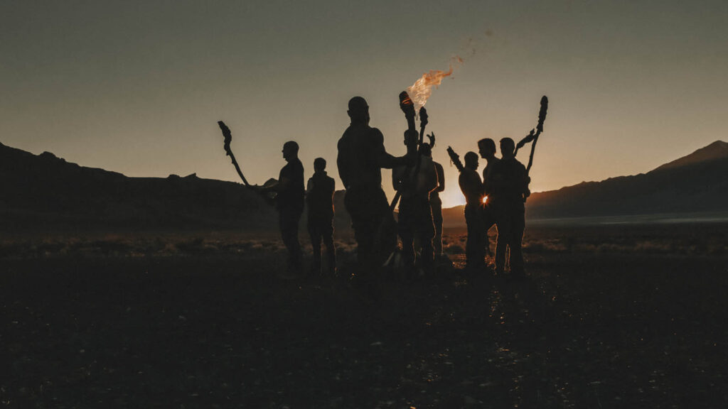 Group of men holding torches in silhouette in a desert valley at dusk